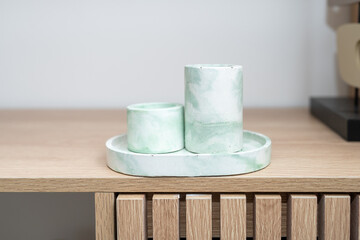 Two concrete candle holders in a light green hue are arranged on a circular tray atop a wooden table. The minimalist design complements the natural wood texture.