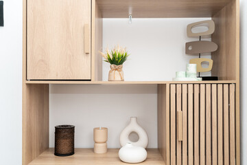 A stylish wooden shelf showcases minimalist decor including vases, a plant, and candle holders, emphasizing a clean, modern aesthetic in a well-lit space.