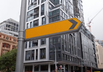 Naklejka premium Yellow arrow sign points toward modern buildings.