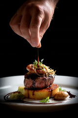 Hand delicately drizzles sauce over gourmet steak dish with potatoes and herbs, beautifully