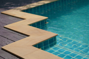 Clear Blue Swimming Pool with Steps and Sunlight Reflections. Related to vacation, leisure, or wellness. Relaxing summer vibe.