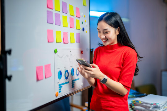 A woman in a red shirt is looking at her cell phone while standing in front of a - Powered by Adobe
