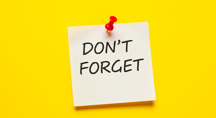 A square sticky note with don't forget written on it attached to a yellow wall with a red push pin