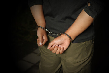 Criminal suspect arrested with hands in handcuff. Dramatic light portrait