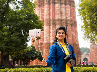 Tourist woman taking selfie in front of Qutub Minar, Delhi, India.