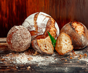 A variety of artisan breads with golden crusts and rustic textures are arranged on a wooden surface, surrounded by scattered flour and crumbs, creating a warm and inviting bakery-style composition.