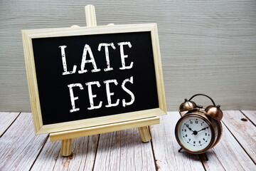 Late Fees text written on chalkboard with alarm clock on wooden background