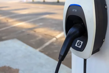 Modern electric vehicle (EV) charger head installed at a designated charging station in an outdoor parking lot, ready for eco-friendly transportation and sustainable energy use. © 2D_Jungle