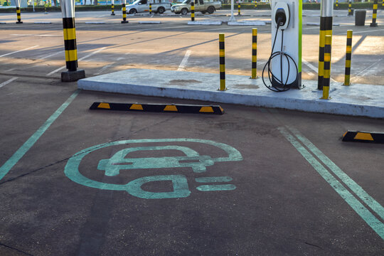 Electric vehicle charging symbol painted on parking lot asphalt. Clear, minimal design indicating EV charging station location.