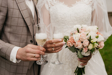 The groom in a brown classic suit and the bride in a white classic fluffy white dress are holding...