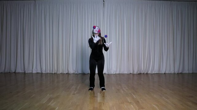 A mime girl juggles circus balls on stage.