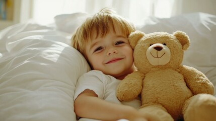 Portrait of little happy toddler boy lying in bed hugging his teddy bear plush toy smiling and daydreaming at peaceful sunny morning