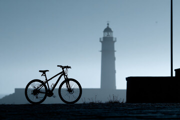 015-043-193-u8969375333_Silhouette_of_a_bike_parked_in_front_of_a_lightho_68ff7fdf-6227-4953-9e0d-08f18f3bb379_0