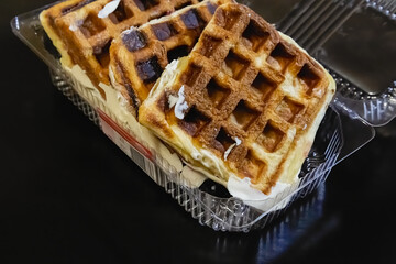 Belgian waffles in a plastic container against a black background