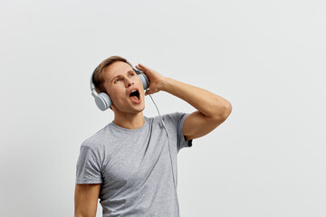 Fototapeta premium Young caucasian man enjoying music with headphones gray t-shirt singing isolated on white background digital detox lifestyle concept