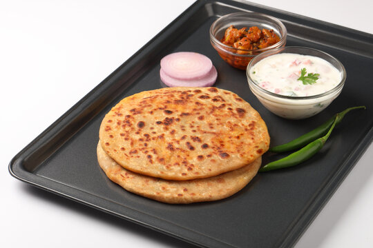 Indian food Aloo Paratha ,Potato stuffed bread served in a black metal tray with raita and mango pickle