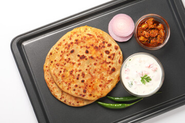Indian food Aloo Paratha ,Potato stuffed bread served in a black metal tray with raita and mango pickle
