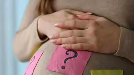 Pregnant woman with question marks on her belly in anticipation of a baby shower gender reveal event concept, pregnancy stage, family planning.