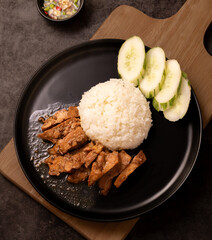 fried pork on rice with cucumber on a black plate, 