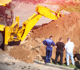Workers stand near a pit with a loader with sand and emergency services in the background. Sewer leak repair, gas service, Close-up