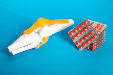 Medical model of knee joint on blue background and stacks of red pills. Concept of chondroprotector drugs for eliminating inflammation and building up cartilage tissue. Copy space for text