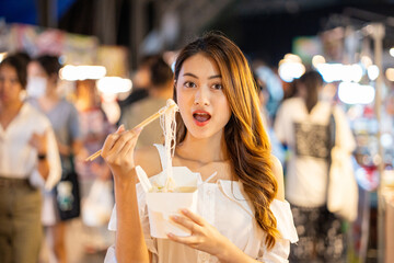 Asian woman enjoy eating noodles street food at night market. Traveler Asian blogger women Happy tourists Beautiful female with Traditional thailand bangkok food.