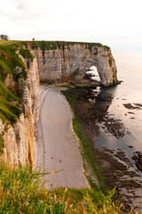 Stunning cliffs tower above the pebble beach in Etretat, France, where boats are anchored. The serene coastline reflects the beauty of nature at sunset.