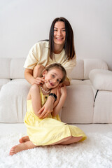 Smiling mother and daughter spending time together playing at home in white room. Family time. Mother's Day.