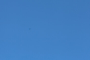 A clear blue sky stretches endlessly, with only a small white airplane flying high above, leaving a barely noticeable trail. Space and tranquility are conveyed by this minimalist shot.