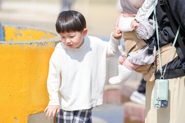 In spring at a park in Fukuoka, a mom in her thirties poses with her 3-year-old son and 6-month-old baby girl. They look at the camera. This photo captures a calm and loving family moment in nature.