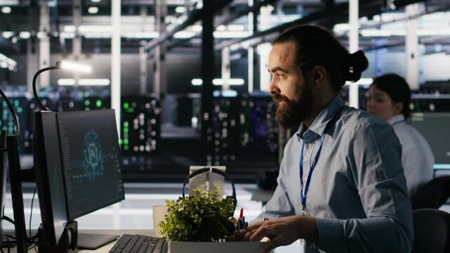 Furious data center engineer packs desk belongings after being replaced by AI automation handling operations. Frustrated man suffering from workforce displacement by artificial intelligence, camera A