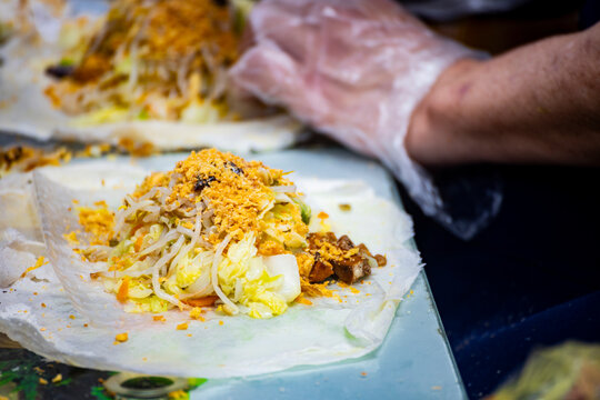 a pair of hands is spreading a rich filling onto a thin popiah skin