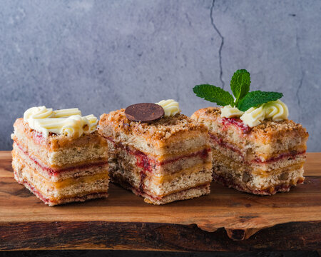 Three pieces of layered cake with cream and berry filling on a wooden board. Close-up, rich texture, clean background.