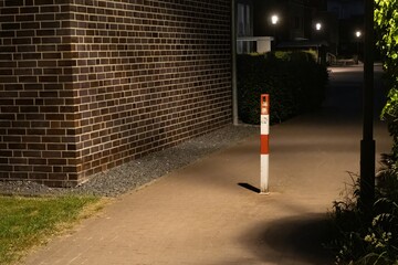 Fototapeta premium Red and white traffic bollard illuminating a sidewalk at night