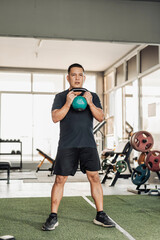 A focused Southeast Asian man in his 50s performs a goblet squat using a green kettlebell at an...