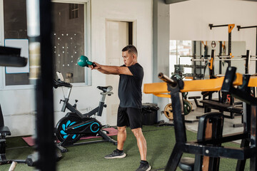 Southeast Asian man in his mid-50s executes a kettlebell swing with precision and effort during his...