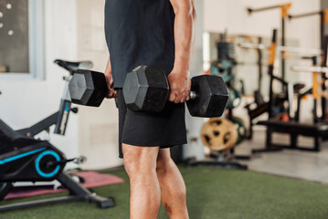 Anonymous man carries two dumbbells in a farmer’s walk for forearm or grip strength and endurance...