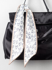 close up thin ribbon scarf with beige hearts pattern   on the black bag