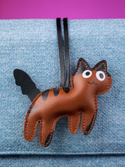 Close up of cute leather keychain in the shape of funny brown  tabby cat on blue  bag