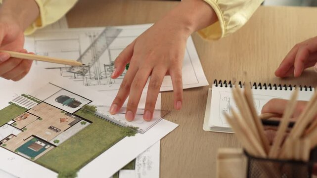 Architects using measurement tool and pencil tracing in building blueprint by coworker support on table with architectural document and wooden block scatter around at office. Closeup. Delineation.