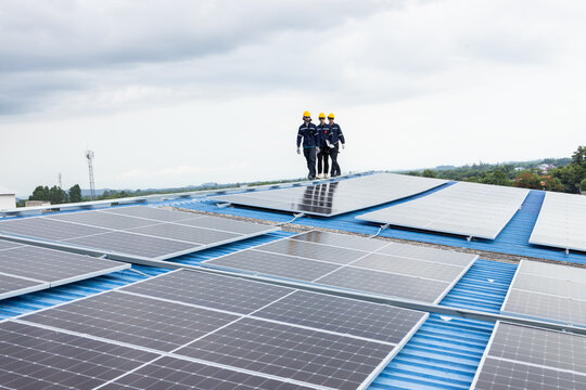 Worker walking inspection solar panels on the roof top of industry building, Large scale of solar energy system for green eco power supply