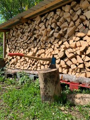 Vertical image of a neatly stacked woodpile with a visible axe handle beside it. The lush green surroundings enhance the calm, rustic mood.