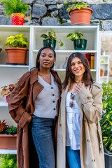 Two young women posing next to a shelf with plants in pots