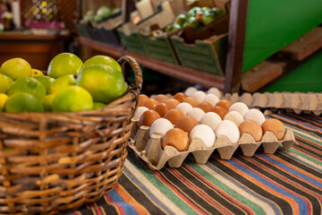 A table has a basket of eggs and a basket of limes. The table is covered with a colorful striped cloth