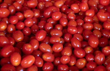 A crate filled with ripe red tomatoes. The crate is made of red plastic and is placed on a table. The tomatoes are arranged in a pile, with some overlapping and others standing upright