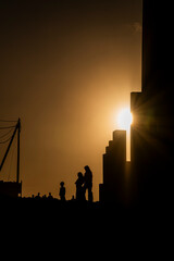 Fototapeta premium A silhouette of a family standing in front of a building. The sun is shining on the building, creating a warm and inviting atmosphere