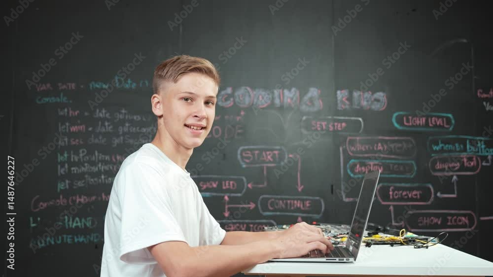 Poster caucasian boy working laptop while looking at camera at blackboard. young high school student progra