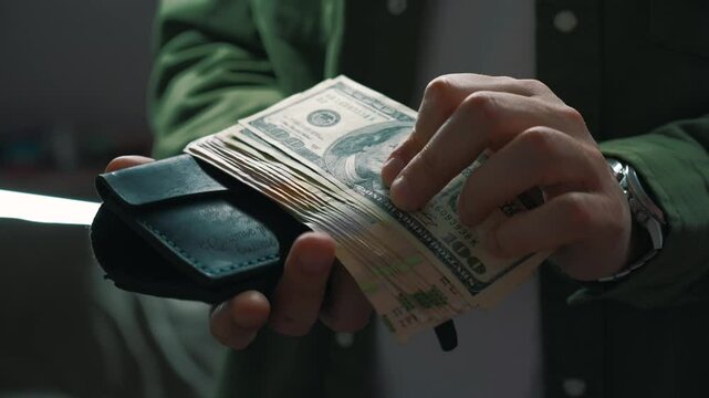 A businessman takes out dollars from his wallet in a dark room.
A man is counting cash that is in his wallet.
Financial director and a lot of money in his wallet