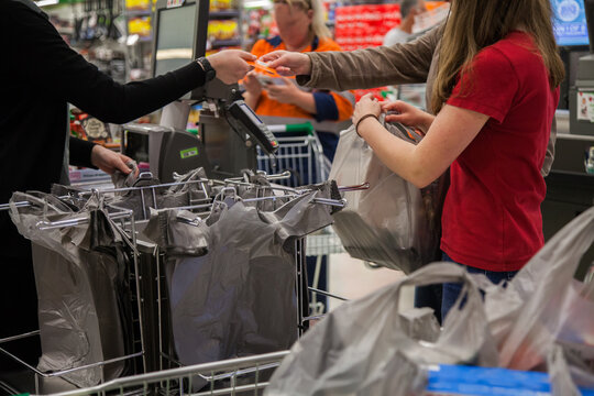Young lady paying for purchases with debit card and packing trolley with shopping