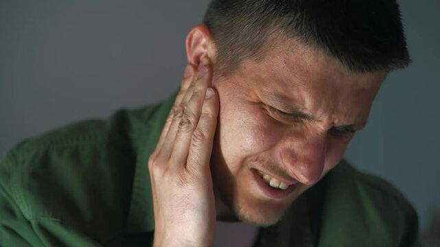 angry european man with glasses experiences ear pain.
A guy in a green shirt touches his sore ear.
Earache in a young guy.
A man massages his ear with his hand to relieve pain.